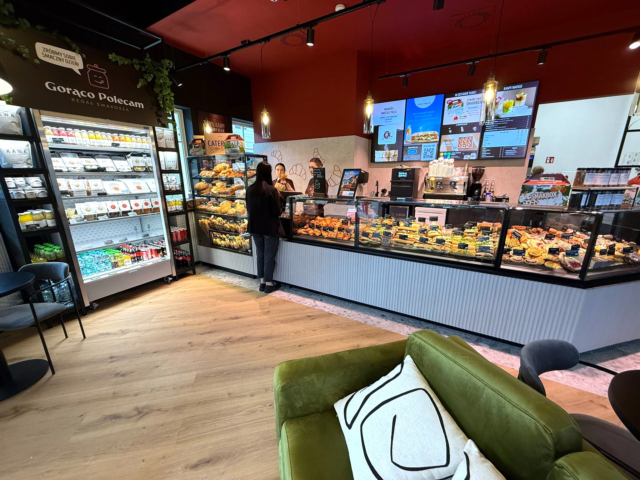 Wnętrze kawiarni Gorąco Polecam z widoczną szeroką ladą pełną świeżych produktów piekarniczych i wyrobów cukierniczych.