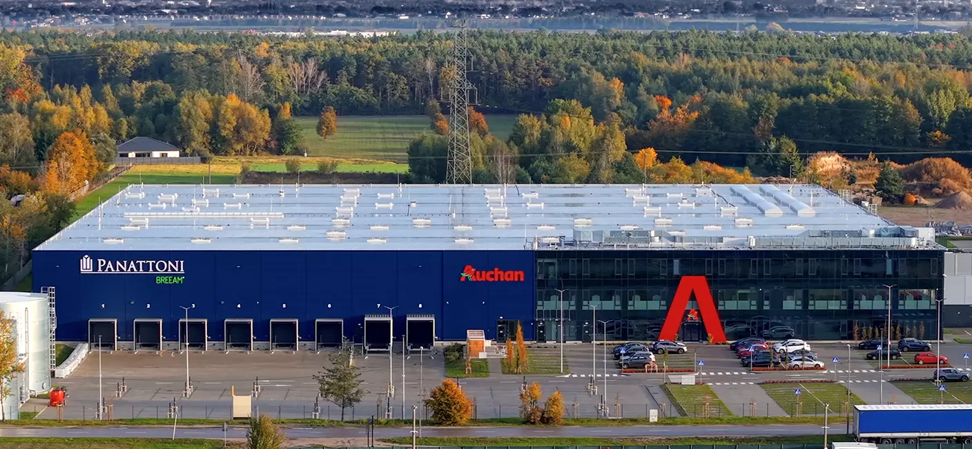 Nowoczesna hala magazynowa Panattoni z logotypem sieci Auchan na tle jesiennego krajobrazu