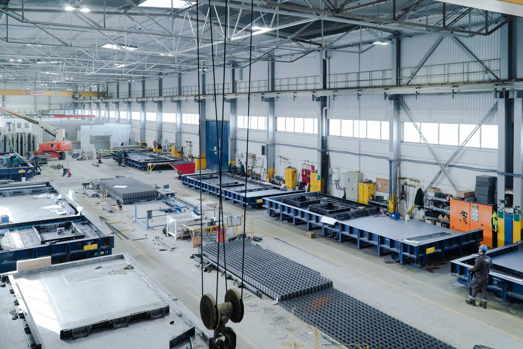 Wnętrze hali produkcyjnej z żółtym dźwigiem suwnicowym i gotowymi betonowymi elementami ścian