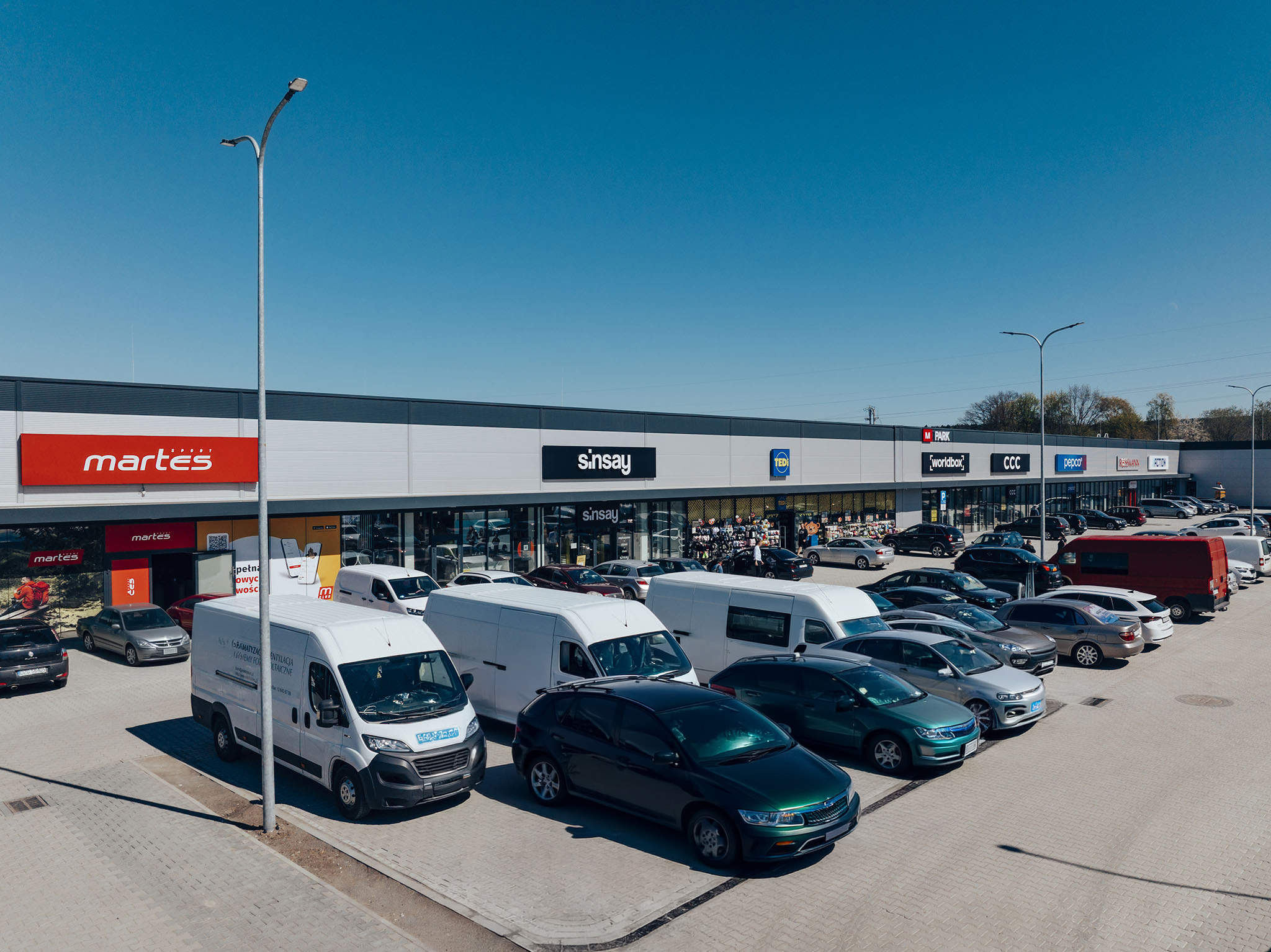 Widok z lotu ptaka na parking i fasadę M Park Bogatynia ze sklepami Martes Sport, Sinsay i Tedi
