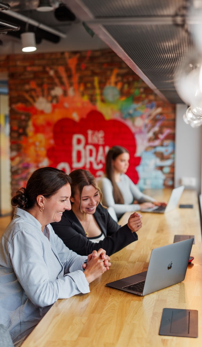 Dwie uśmiechnięte kobiety pracujące przy laptopie w nowoczesnym biurze coworkingowym