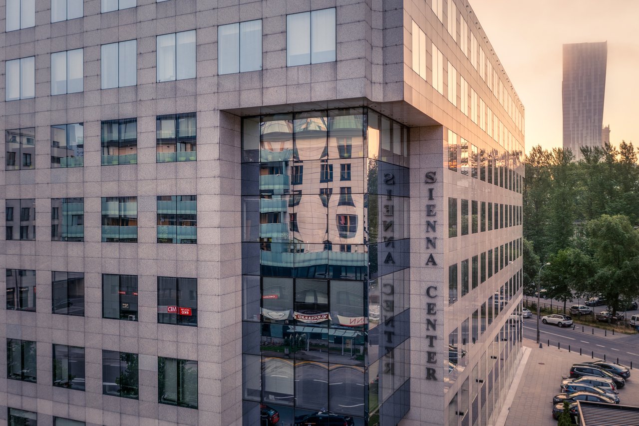 Ulica w centrum Warszawy z widokiem na nowoczesny budynek Siena Center i otaczające go wieżowce.