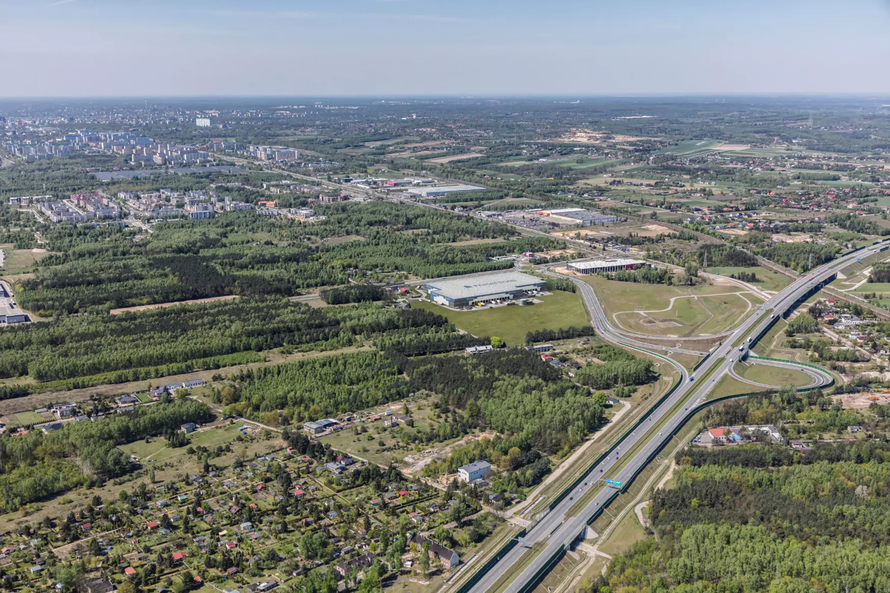Rzędy palet z towarami w nowoczesnej hali magazynowej, oświetlonej naturalnym światłem i sztucznym oświetleniem LED.