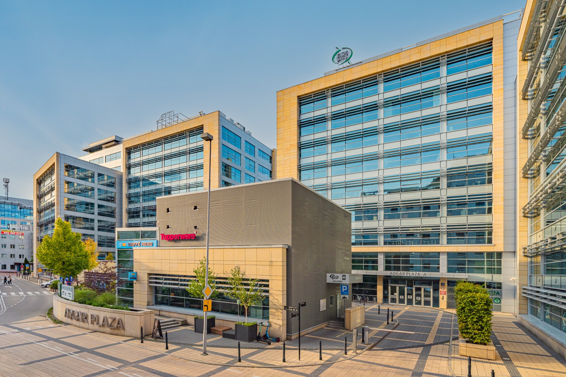 Kompleks nowoczesnych biurowców Adgar Plaza A i B z przeszklonymi elewacjami i pawilonem parterowym z napisem „ADGAR PLAZA” na dziedzińcu.
