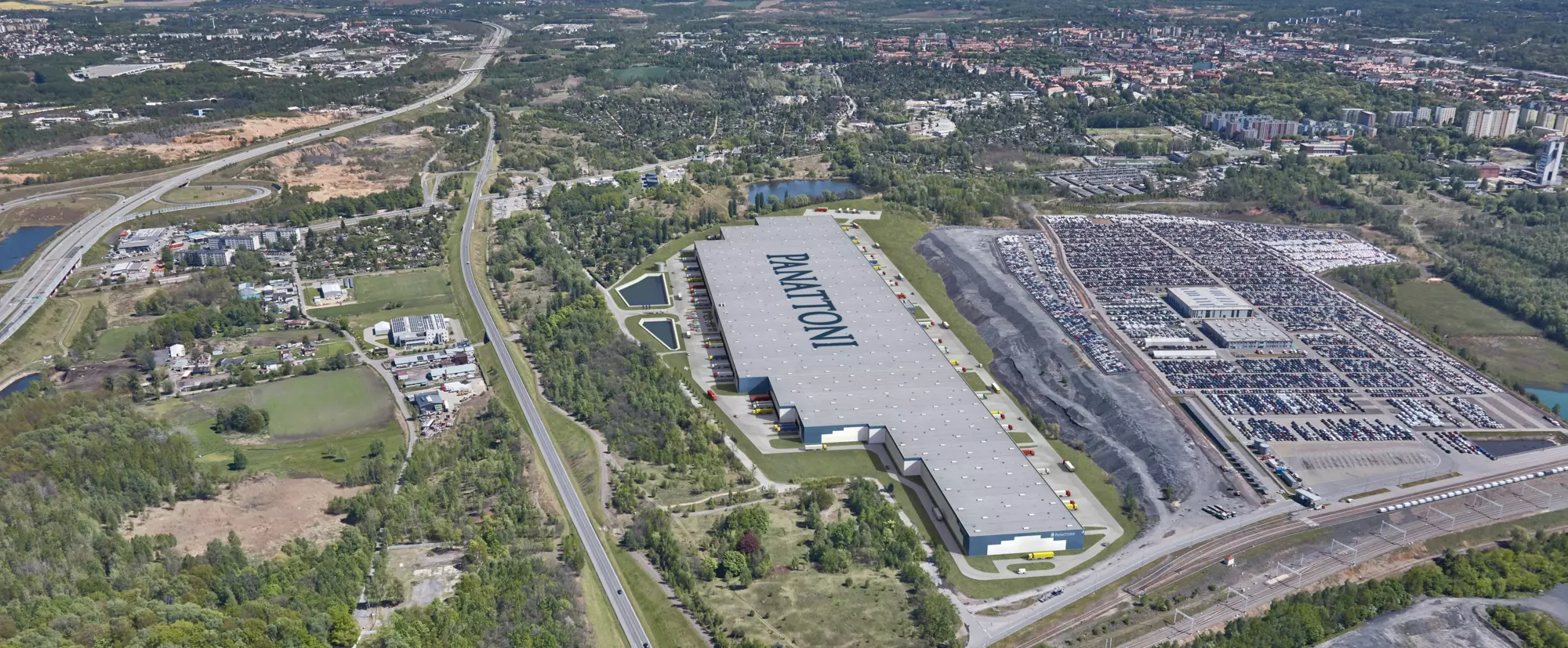 Rozległe centrum logistyczne z dużą, szarą halą magazynową oraz rozległym placem parkingowym i drogą szybkiego ruchu.
