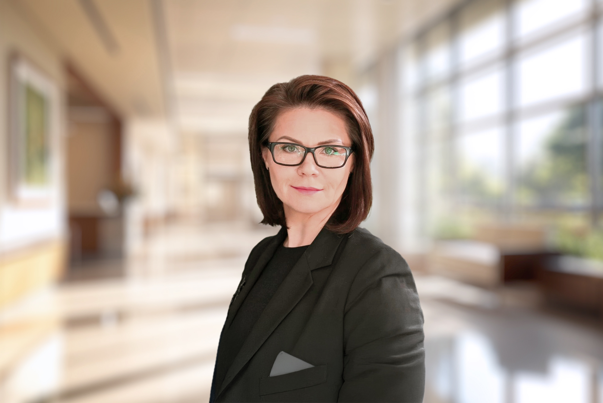 Portret kobiety w średnim wieku o ciemnych, prostych włosach do ramion, ubranej w czarną marynarkę i okulary.