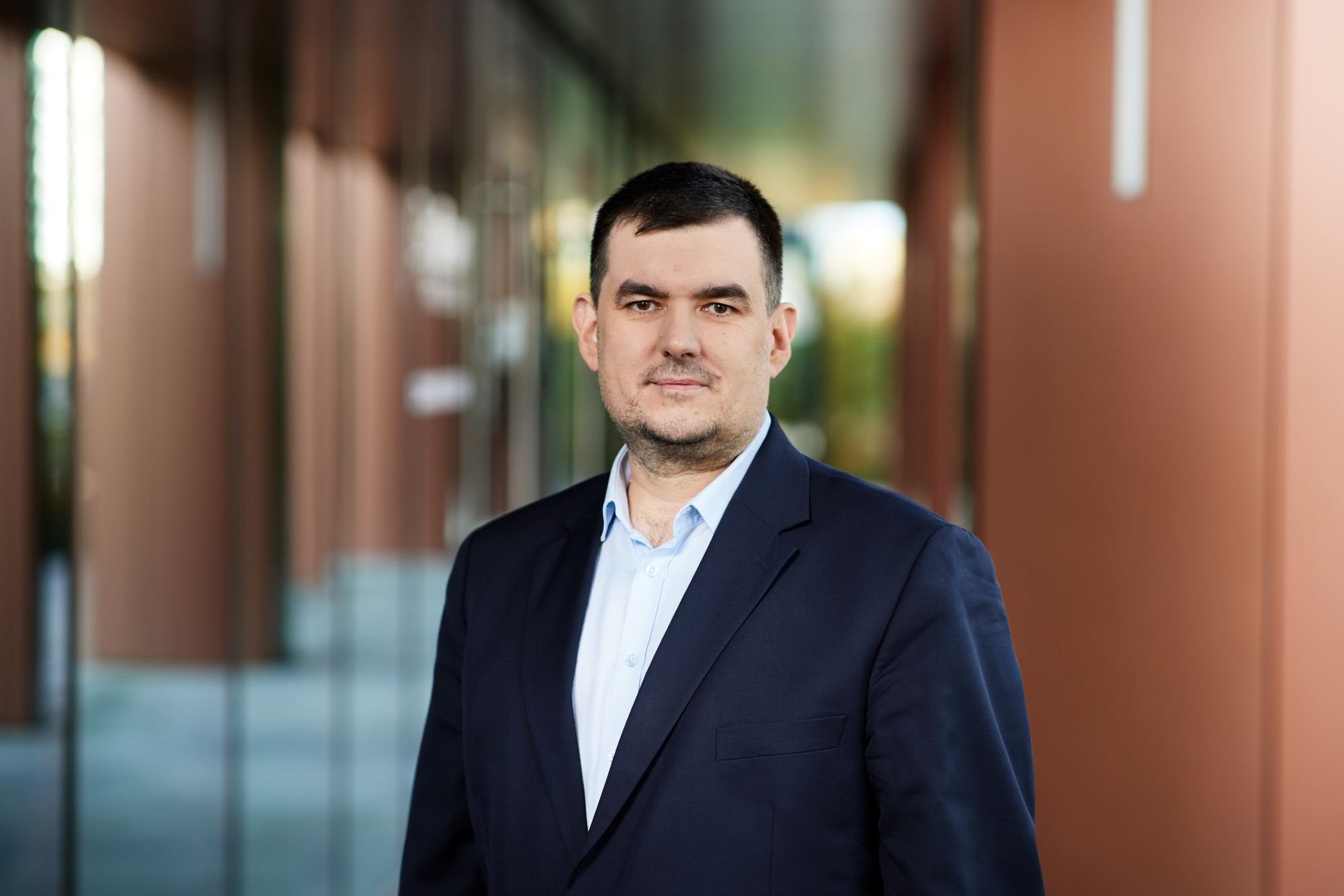 Mężczyzna w średnim wieku z krótkimi, ciemnymi włosami i lekkim zarostem pozuje do portretu biznesowego w granatowej marynarce.