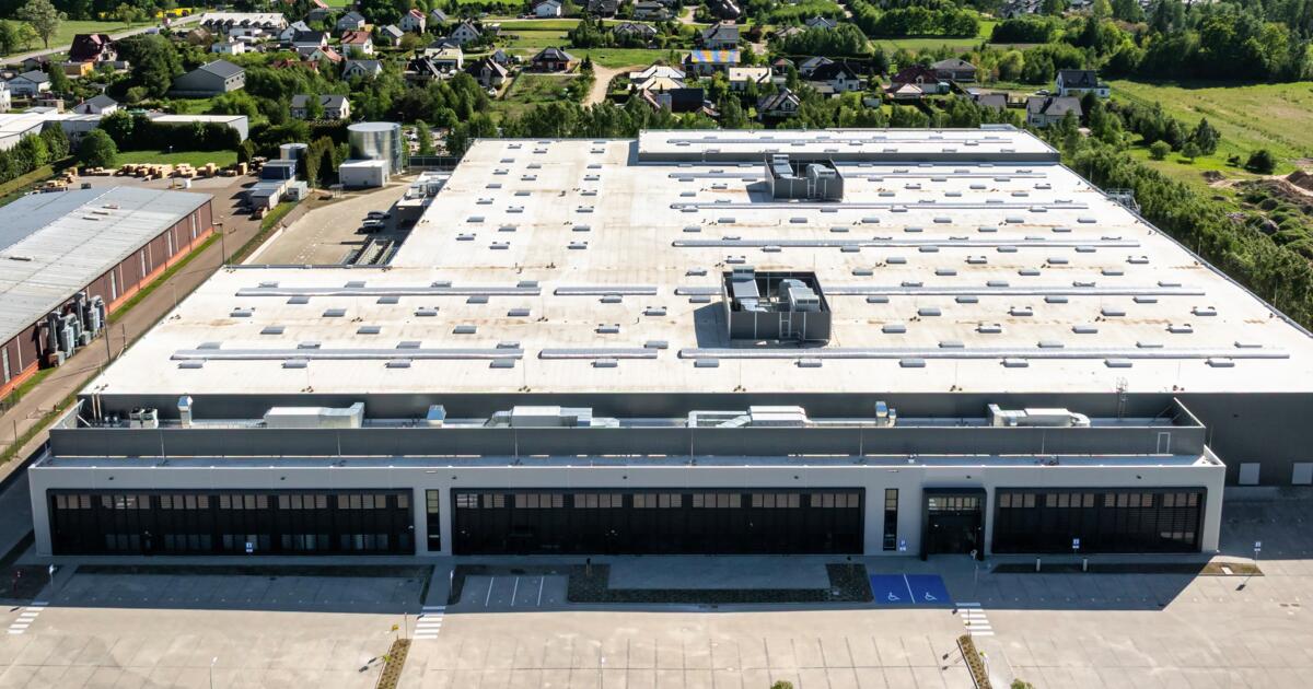 Z lotu ptaka nowoczesna hala magazynowo-produkcyjna z jasnym dachem, parkingiem i otoczeniem domów jednorodzinnych.