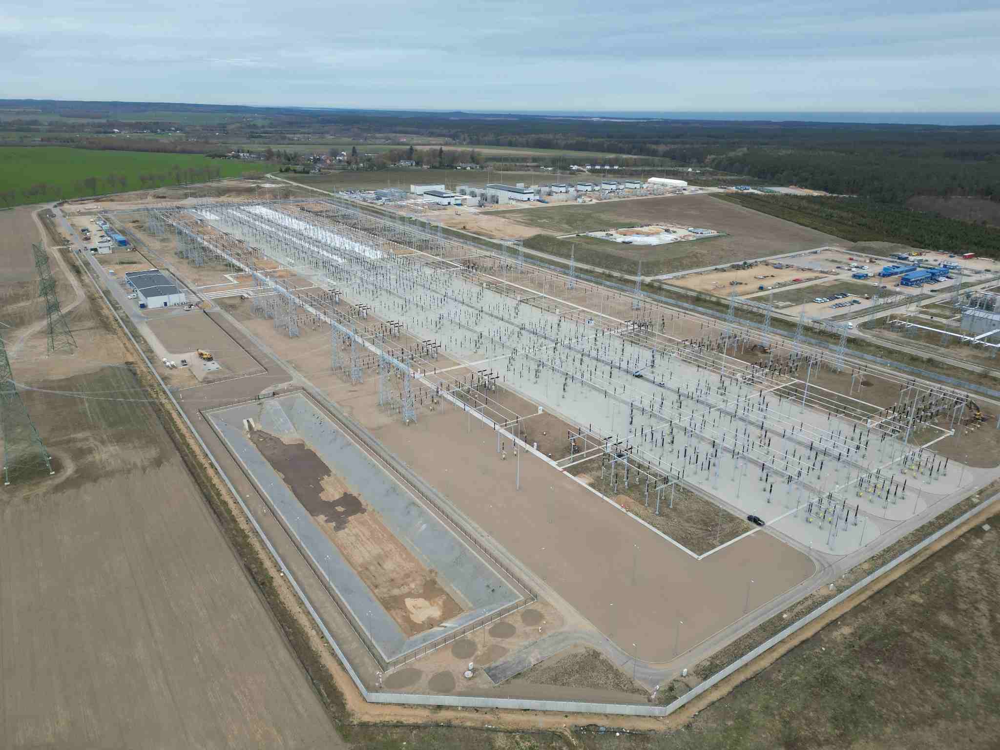 Widok z lotu ptaka przedstawia rozległą stację elektroenergetyczną z gęstą siecią stalowych konstrukcji i szyn przesyłowych.