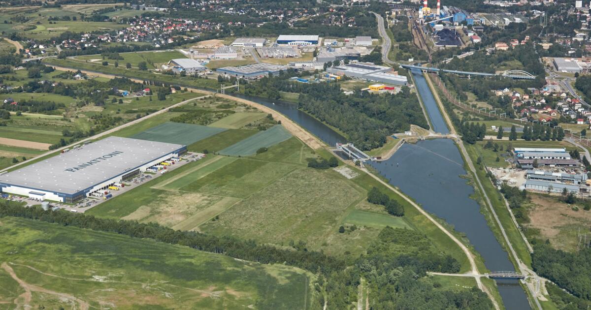 Zdjęcie lotnicze przedstawia rozległy teren przemysłowo-logistyczny nad kanałem wodnym, z halą magazynową PANATTONI, zielonymi polami i infrastrukturą.