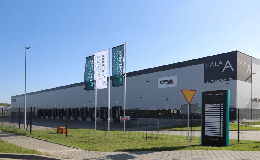 Nowoczesna hala magazynowo-logistyczna z dokami przeładunkowymi, trzema flagami firmowymi Fortress Logistics i pylonem informacyjnym.