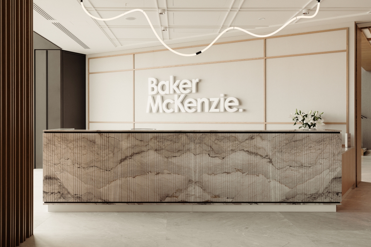Nowoczesna recepcja biurowa z kamienną ladą, na którą pada światło z falistej instalacji świetlnej pod sufitem. Na ścianie napis „Baker McKenzie”.
