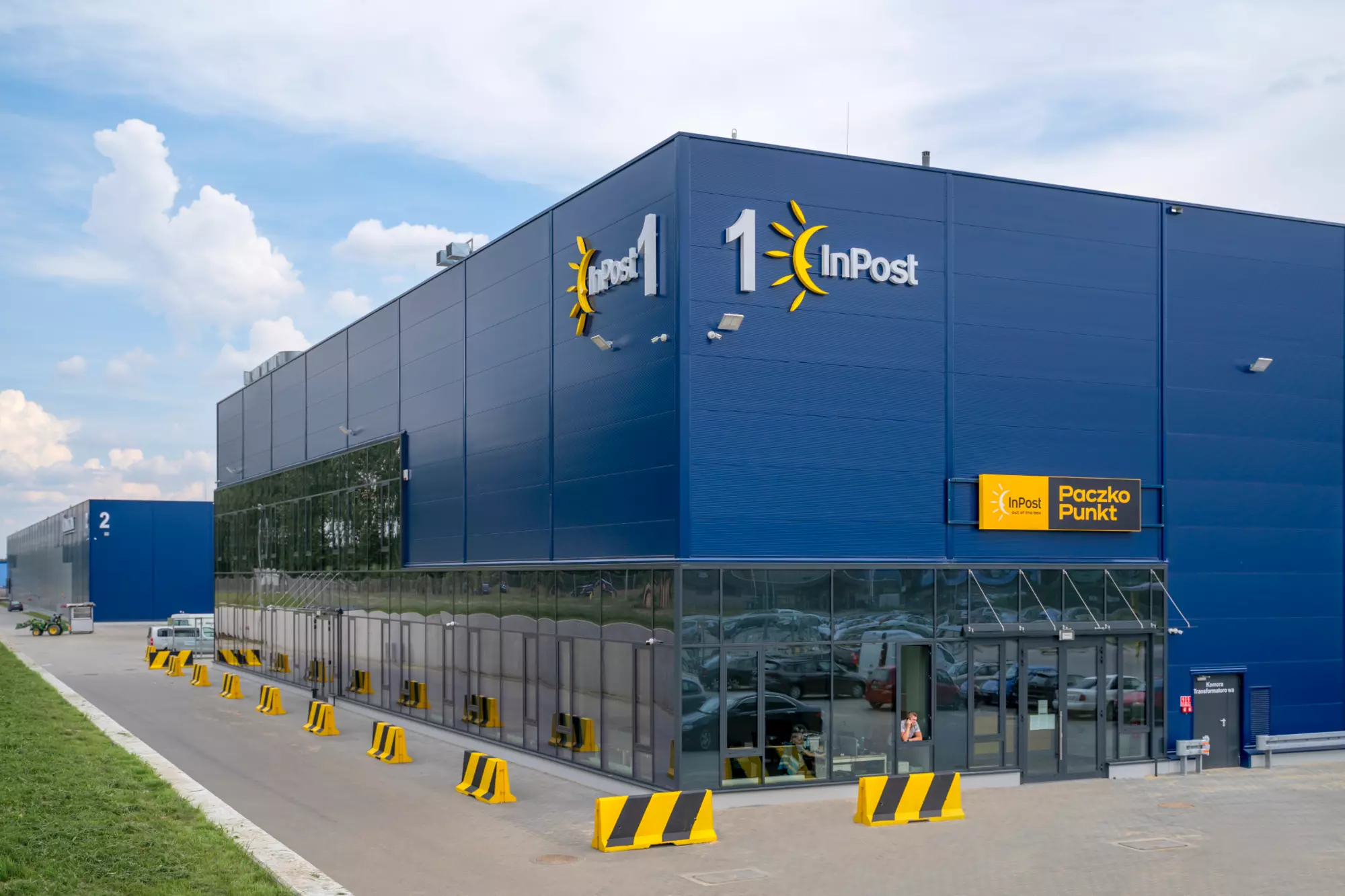 Nowoczesny, wielkogabarytowy budynek magazynowo-biurowy z granatową elewacją i przeszklonym parterem. Widoczne logo InPost obok wejścia.