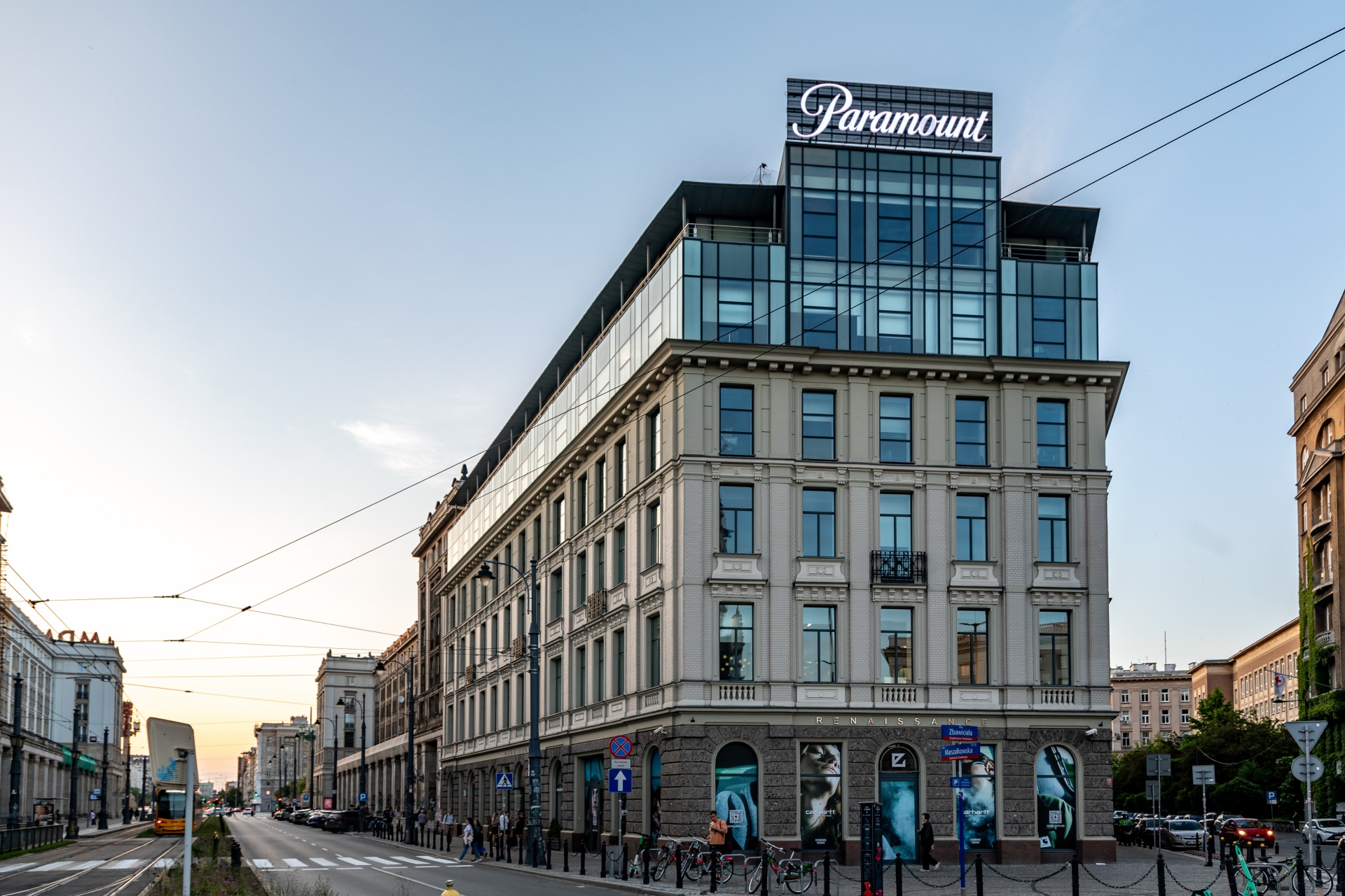 Wielopiętrowy, narożny budynek w miejskim krajobrazie łączy klasycystyczną fasadę z nowoczesną szklaną nadbudową i neonem „Paramount”.