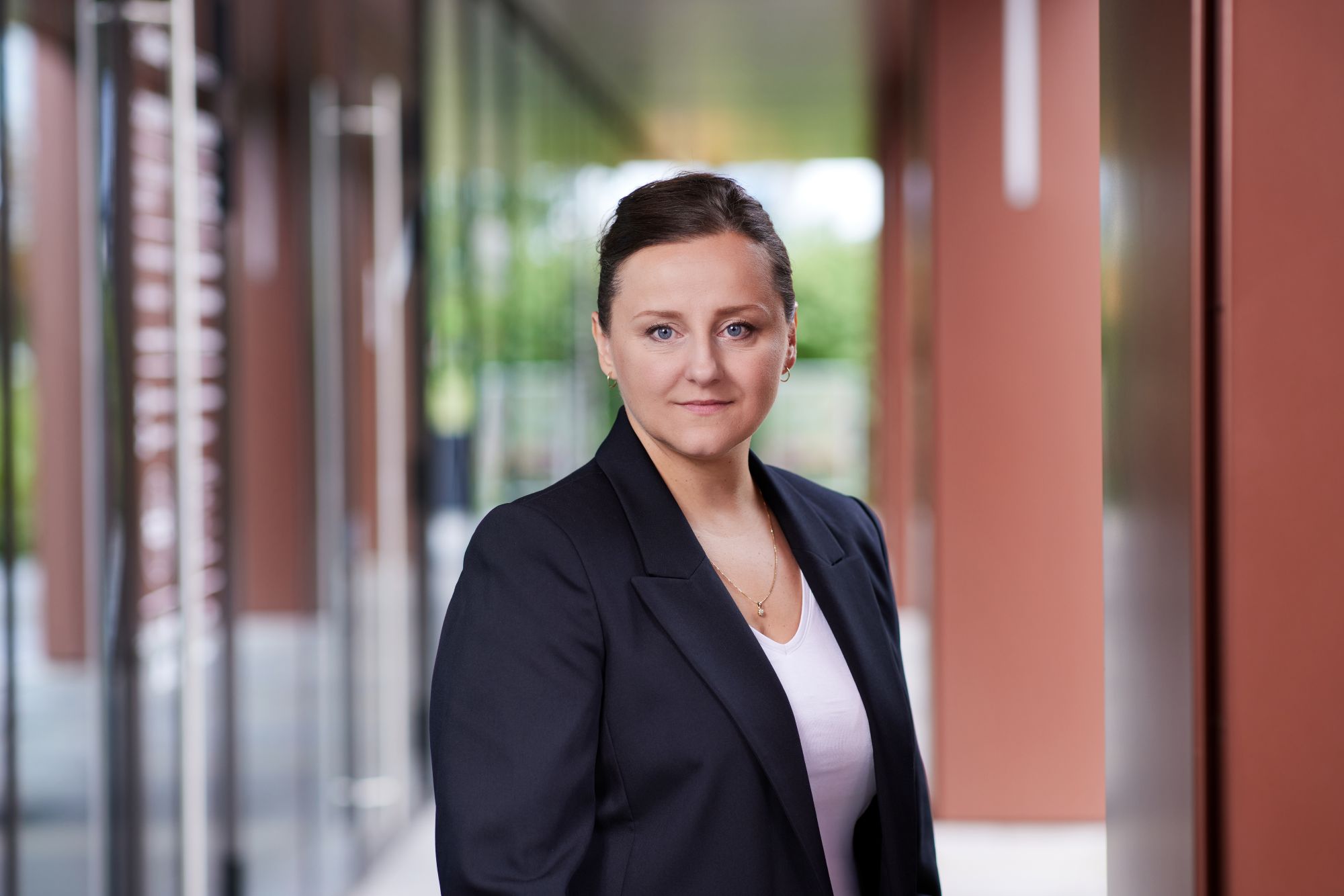 Portret dojrzałej kobiety z ciemnymi, upiętymi włosami i niebieskimi oczami, w granatowej marynarce.