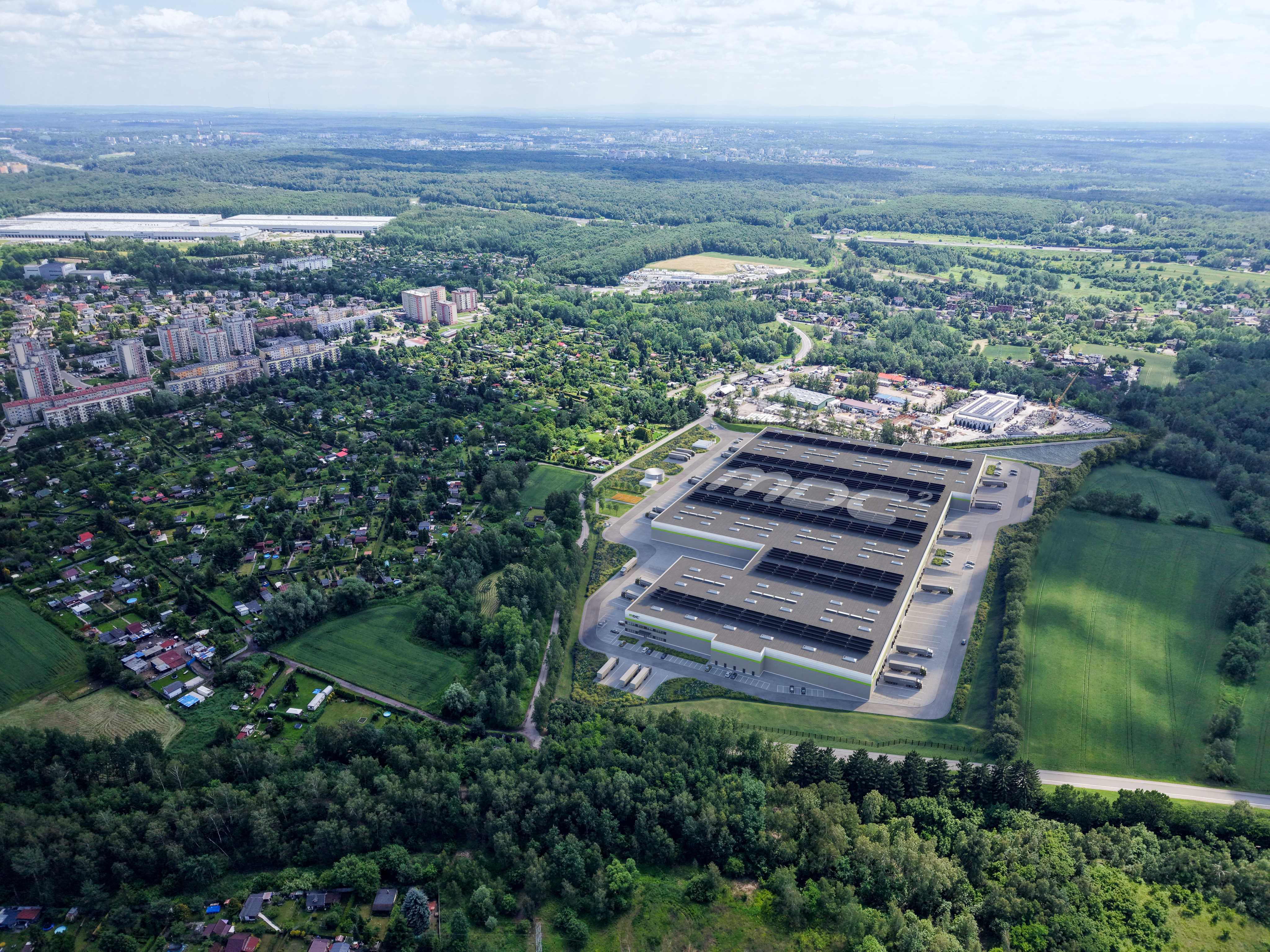 Zdjęcie lotnicze przedstawia nowoczesny kompleks logistyczno-magazynowy z ciemnym dachem MDC2 otoczony parkingami, zielenią i lasem.