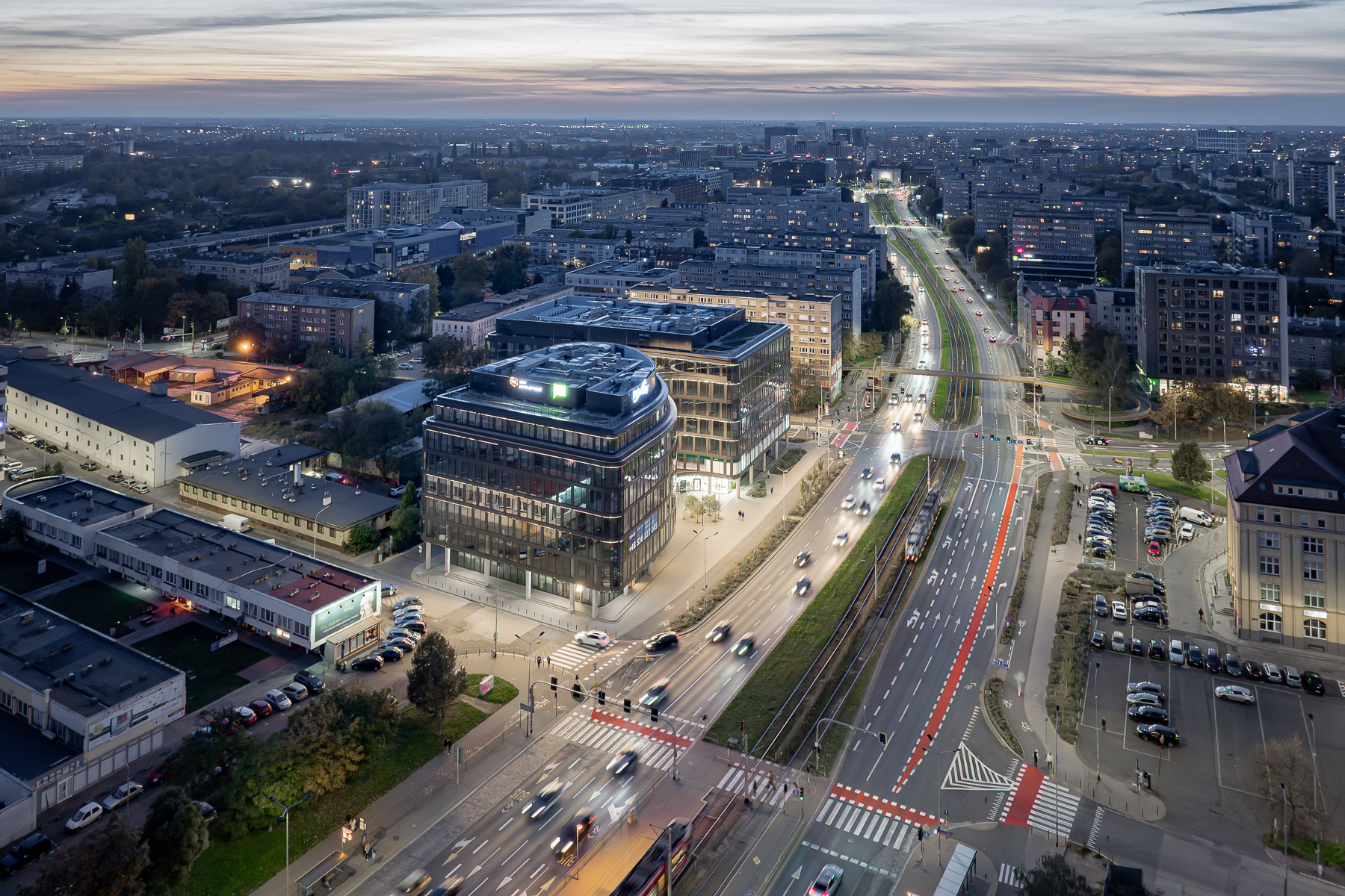 Panorama miasta o zmierzchu ukazuje nowoczesny biurowiec Infinity o zaokrąglonej bryle z przeszkloną fasadą.