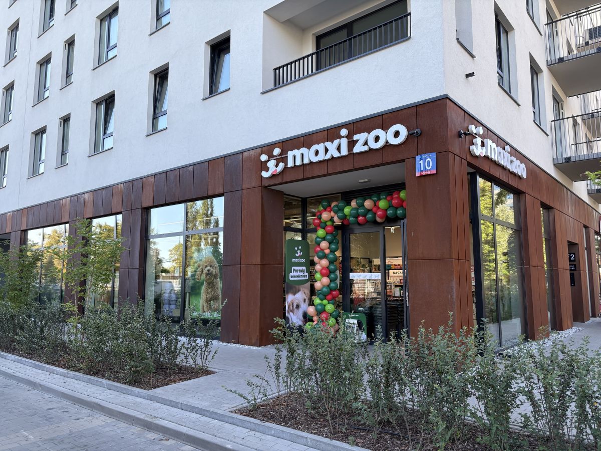 Widok zewnętrzny narożnego lokalu Maxi Zoo w nowoczesnym białym budynku z panelami w kolorze rdzawej miedzi.
