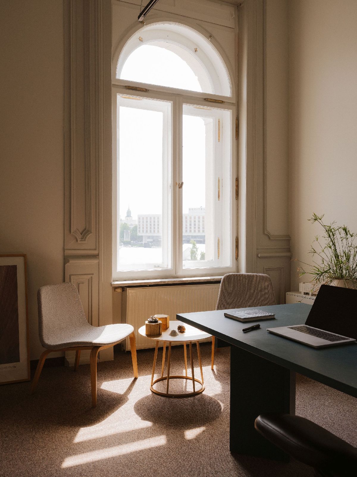 Jasne, minimalistyczne wnętrze biurowe z wysokim, łukowatym oknem wychodzącym na architekturę miejską.