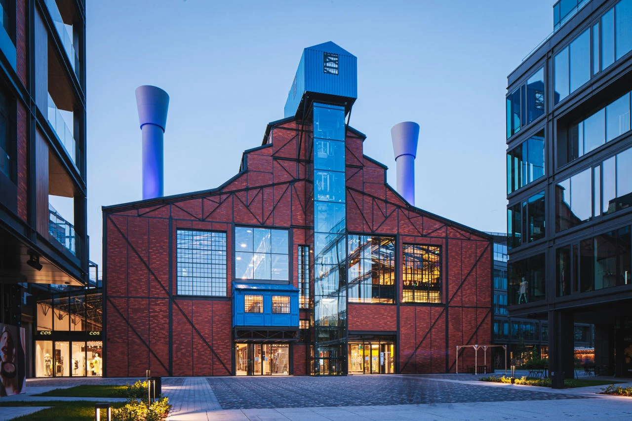 Odrestaurowany industrialny budynek z czerwonej cegły i czarnej konstrukcji stalowej, z dużymi przeszkleniami.