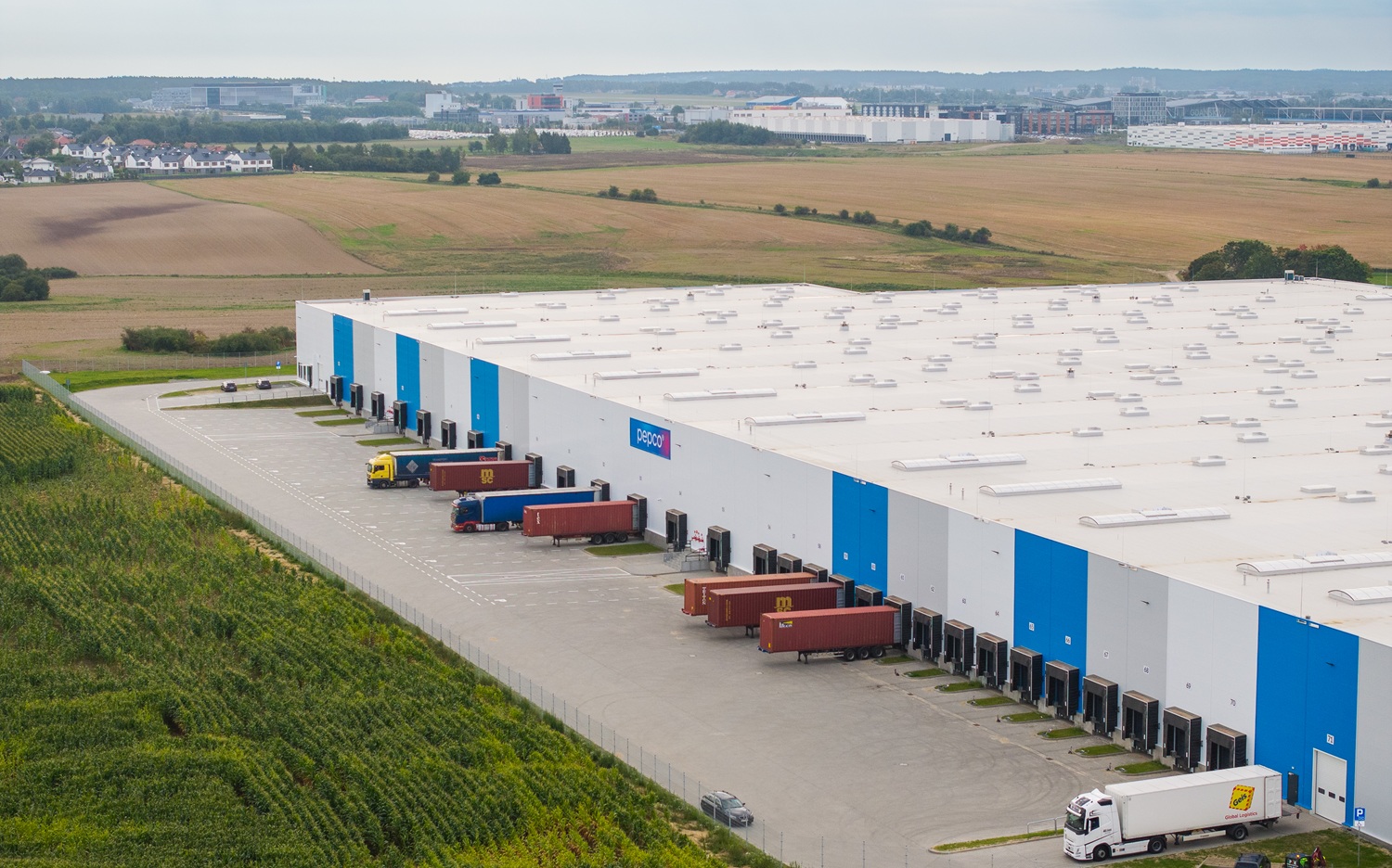 Widok lotniczy na ogromne centrum logistyczne Pepco o białej elewacji z niebieskimi pasami i licznymi bramami przeładunkowymi.