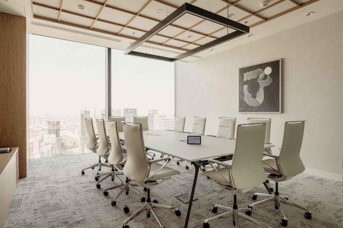 Nowoczesna sala konferencyjna z białym stołem, ergonomicznymi fotelami, przeszkloną ścianą z panoramą miasta.