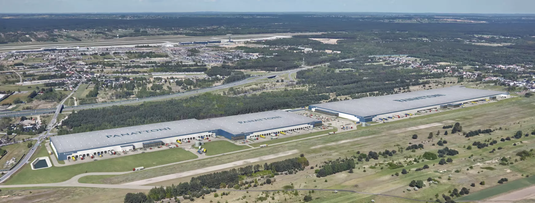 Panoramiczny widok z lotu ptaka na dwa rozległe centra logistyczne Panattoni z dokami przeładunkowymi i ciężarówkami.