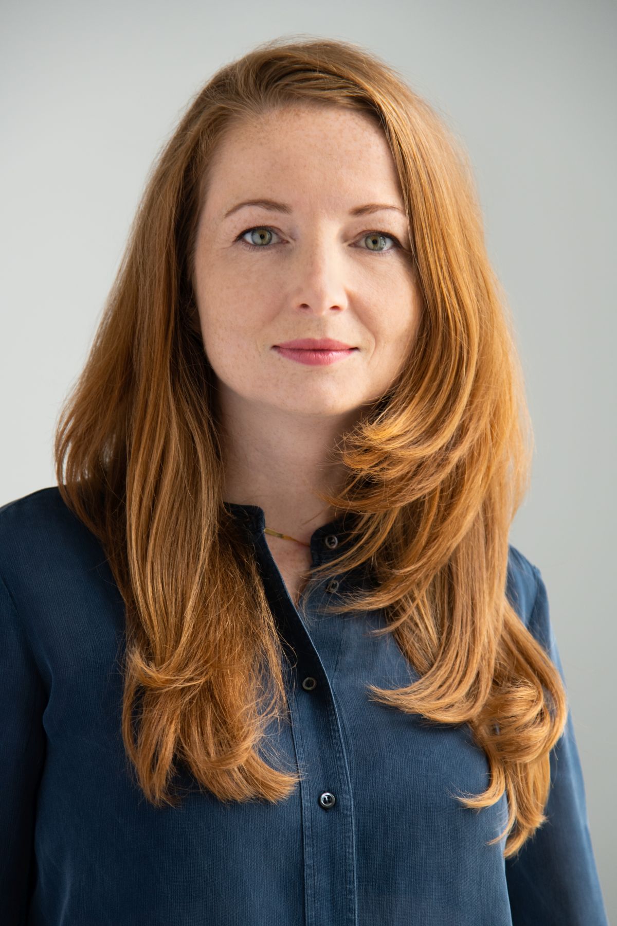 Portret dorosłej kobiety z rudymi włosami, uśmiechniętej, w ciemnoniebieskiej koszuli.