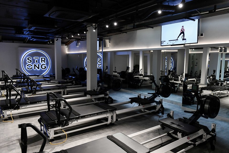 Nowoczesna sala do ćwiczeń z rzędami biało-czarnych maszyn do pilatesu typu reformer i lustrzaną ścianą.