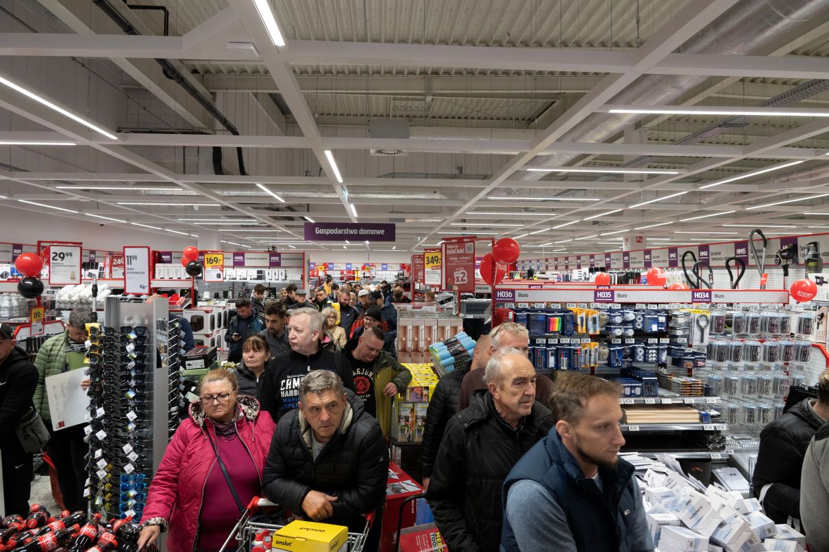 Wnętrze dużego multimarketu Jula, gdzie tłum ludzi stoi w długiej kolejce, otoczony regałami z artykułami gospodarstwa domowego i narzędziami.