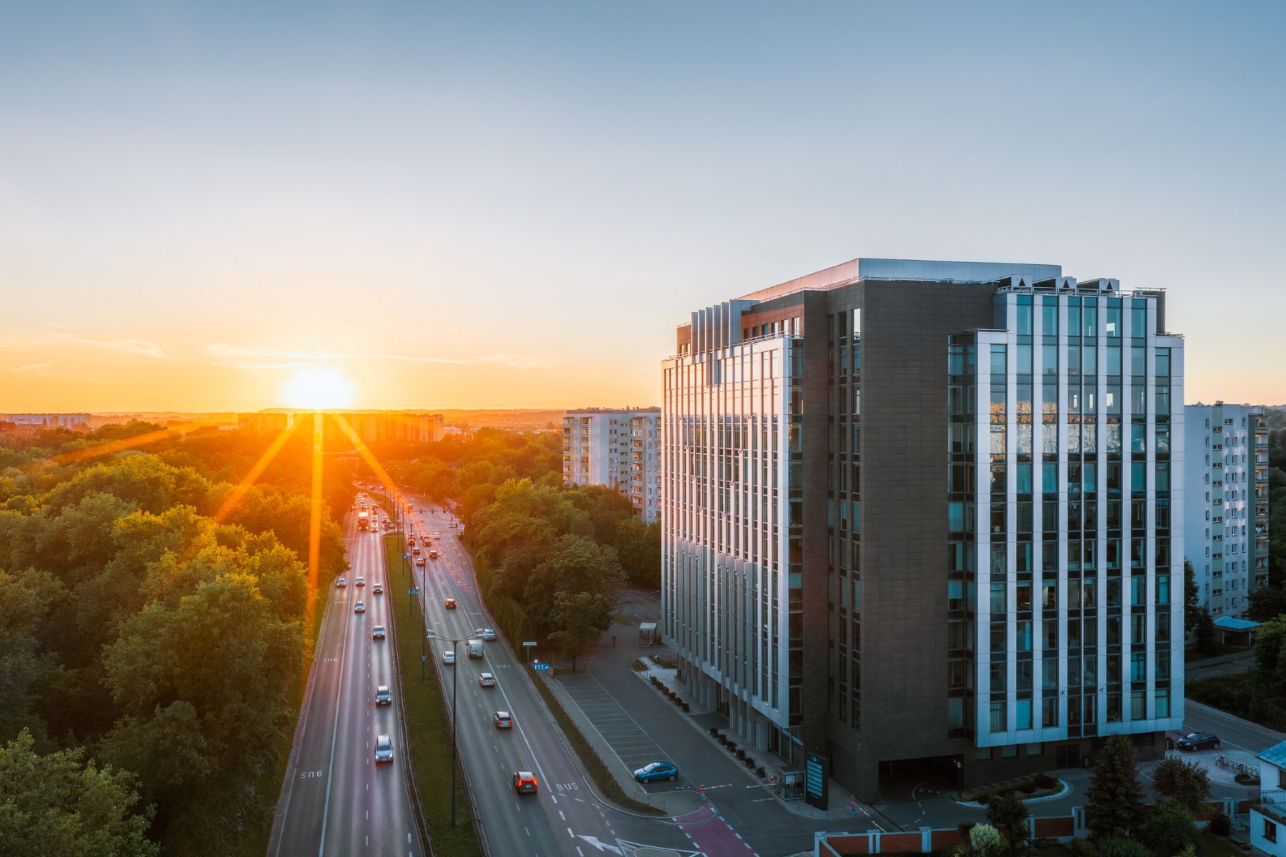 Nowoczesny, wielopiętrowy biurowiec z przeszkloną fasadą i kamienną elewacją obok arterii komunikacyjnej.