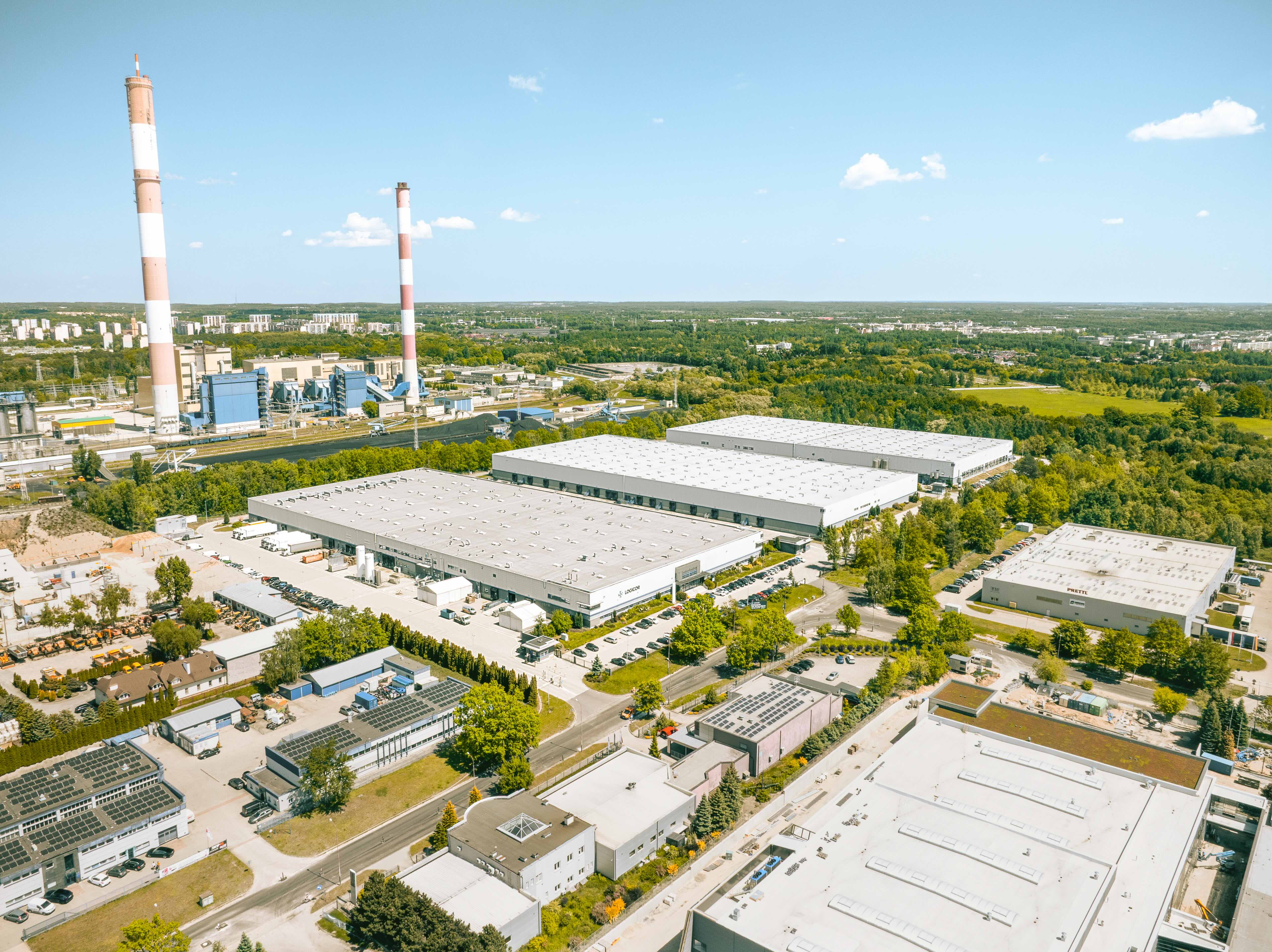 Widok z lotu ptaka na rozległy kompleks hal logistycznych Logicor Łódź z dwoma wysokimi kominami i parkingami.
