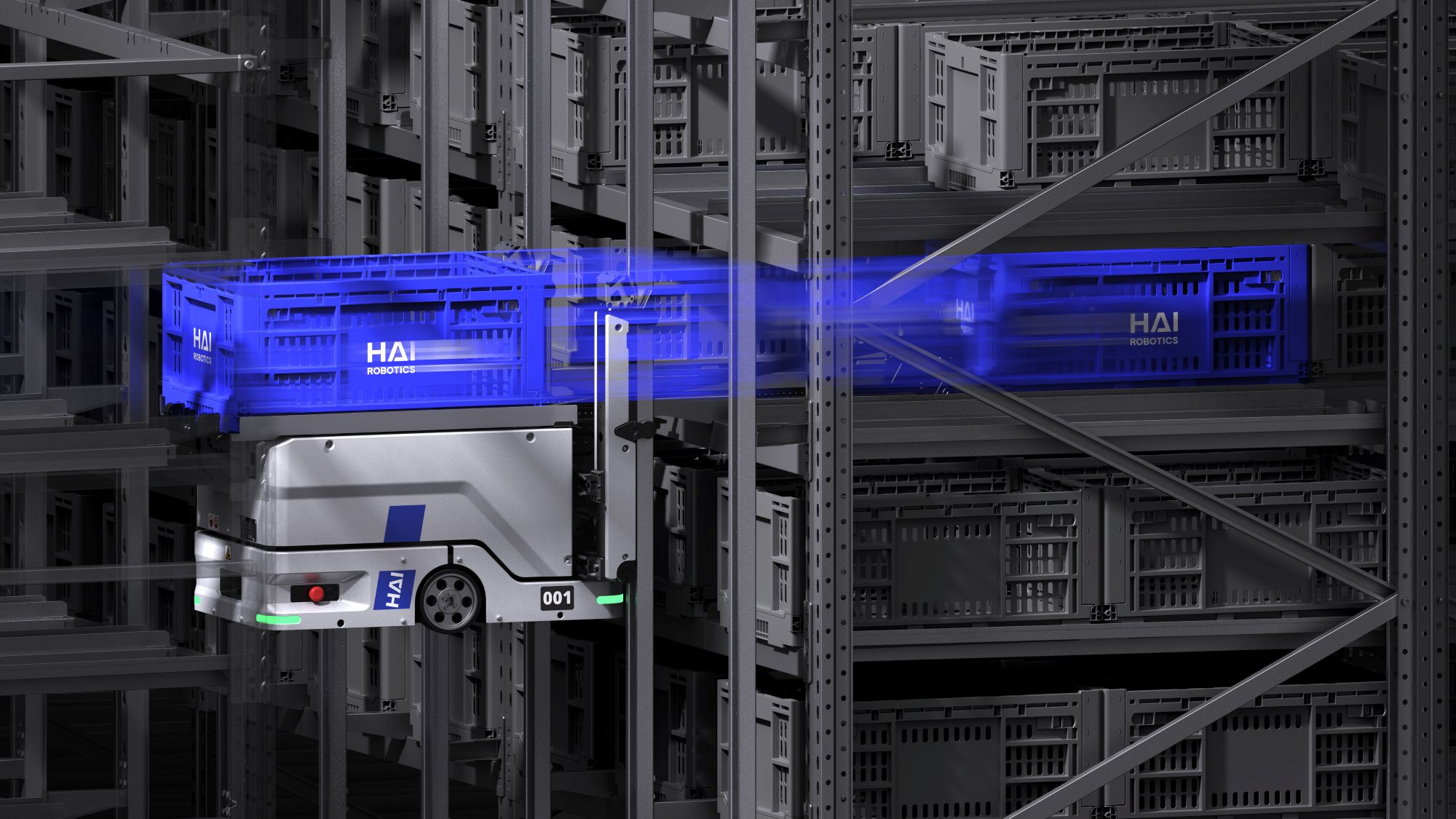 Srebrny, zrobotyzowany pojazd magazynowy z niebieskimi akcentami porusza się wzdłuż wysokiego regału wypełnionego szarymi skrzyniami, transportując niebieską skrzynię z napisem HAI ROBOTICS.
