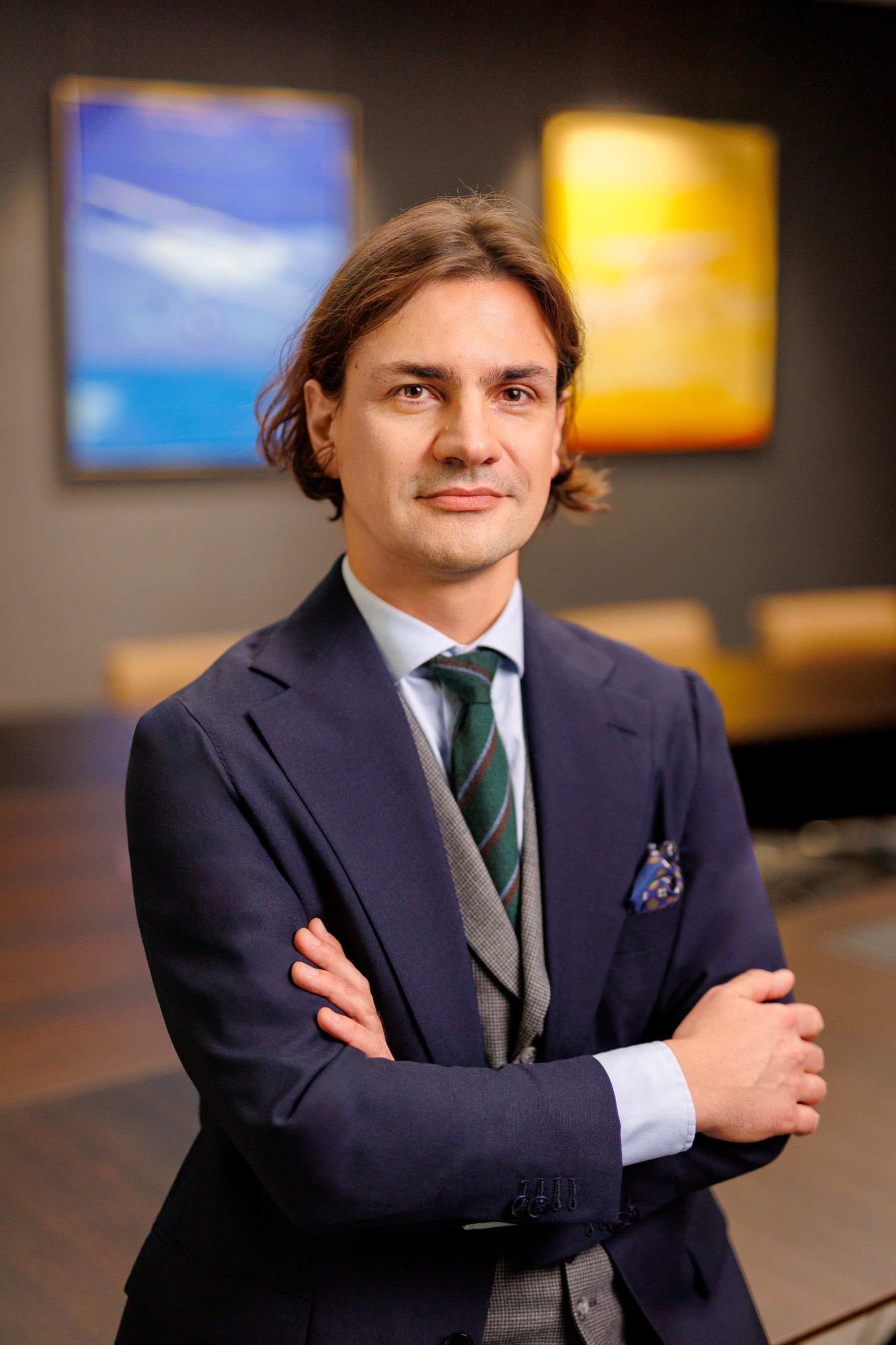 Portret uśmiechniętego mężczyzny o brązowych włosach, w garniturze i krawacie, stojącego na tle biura.