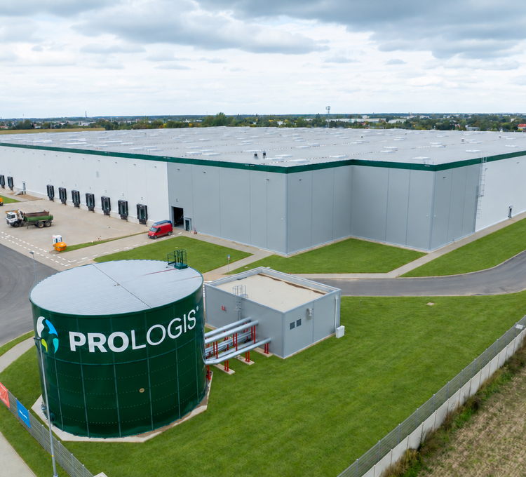 Widok zewnętrzny hali magazynowej z dokami oraz zielonym zbiornikiem z logo Prologis i stacją pomp.