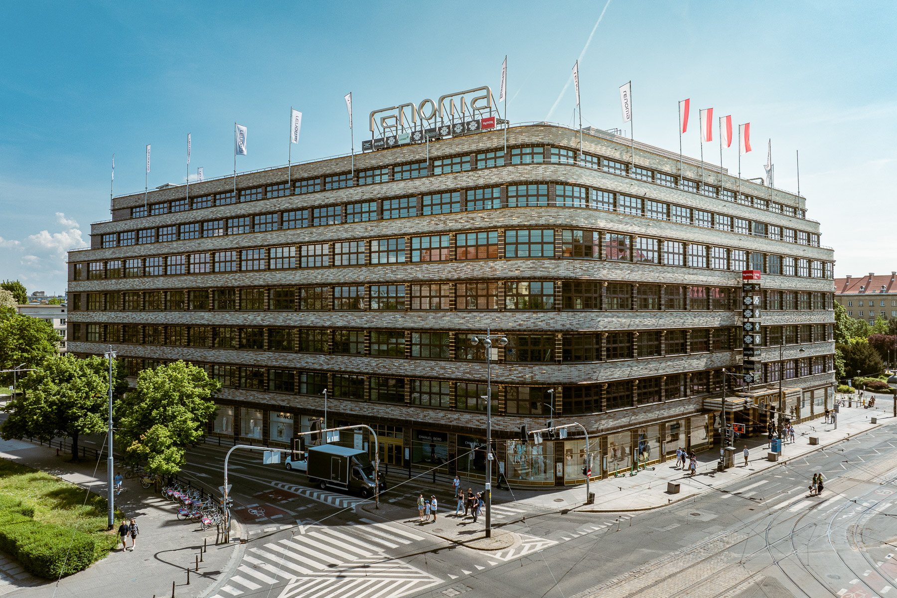 Modernistyczny gmach wrocławskiego domu towarowego Renoma z zaokrąglonym narożnikiem, widoczny od strony skrzyżowania w słoneczny dzień.