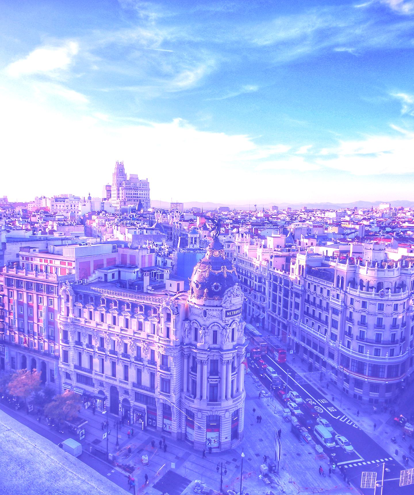Luchtfoto van een drukke stadsstraat met het Metropolis Building en de omliggende architectuur onder een blauwe lucht met verspreide wolken.