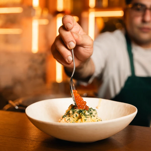 Example of social media content - Chef adding red fish roe garnish with a spoon to a creamy, herb-topped dish in a white bowl.