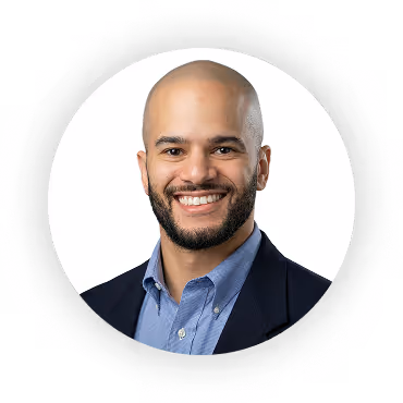 Smiling bald man with a beard wearing a blue dress shirt and dark blazer against a white background.
