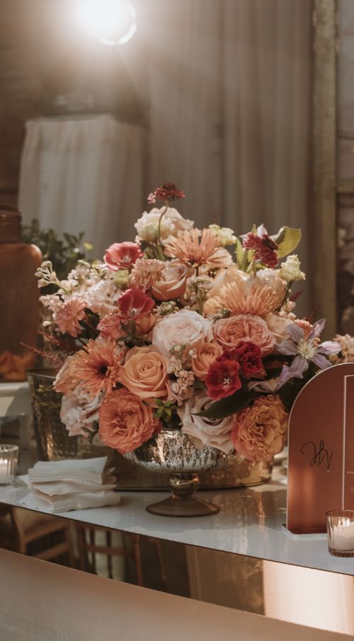 Cream and pastel floral centerpiece at luxury wedding reception bar, highlighted by professional event lighting from Contak AV
