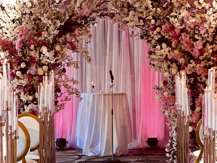 Wedding aisle with tall gold candelabras and floral arch at Hotel William Gray in Old Montreal, with white sheer backdrop and ceremony microphone
