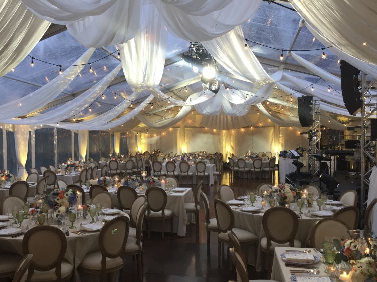 Montreal outdoor wedding setup with candlelit tables, clear top tent, draped ceiling, vintage string lights, and full AV stage rig