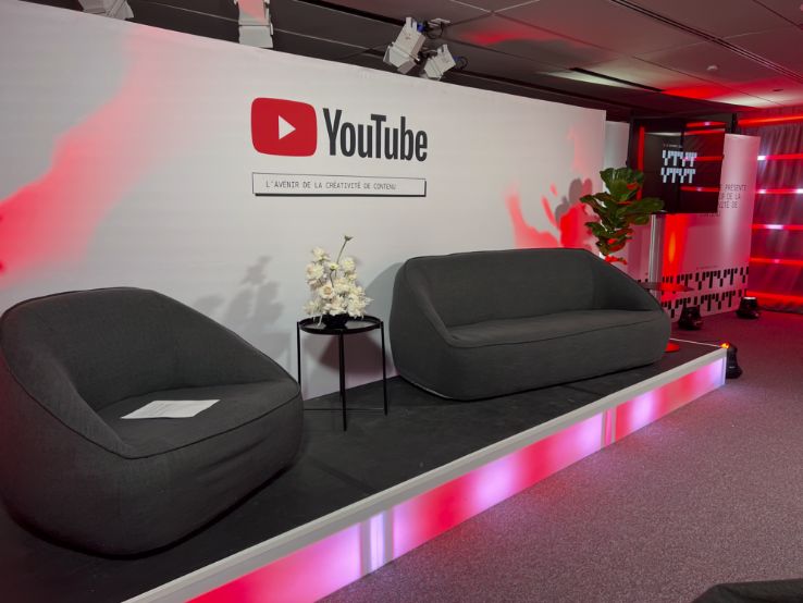 Hybrid YouTube broadcast set with LED tube decor, two modern couches, professional uplighting, and stage lighting for livestream events