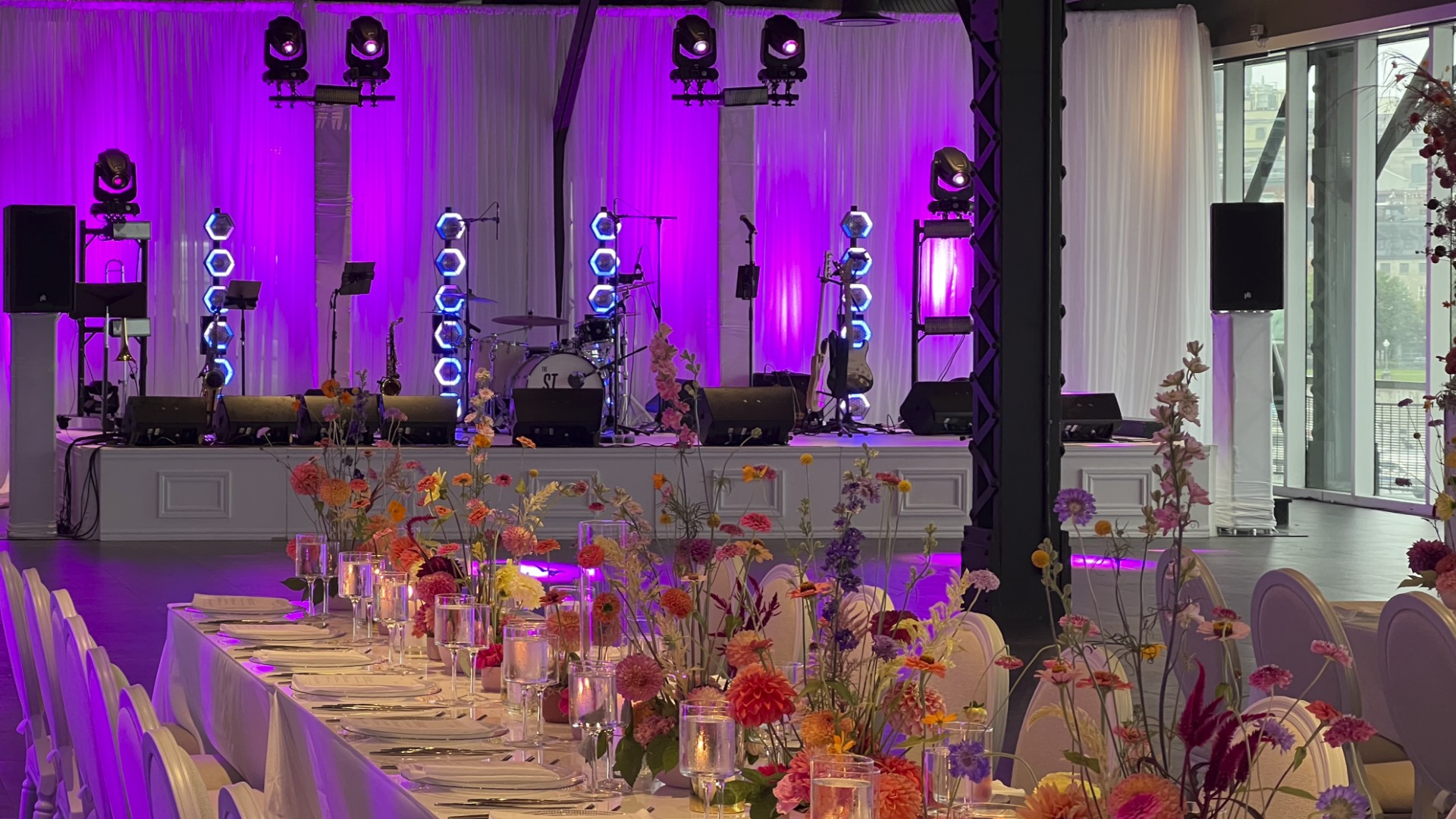 Elegant wedding stage setup with white sheer curtains, purple dance floor lighting, and colorful floral centerpieces at the Montreal Science Centre Belvedere