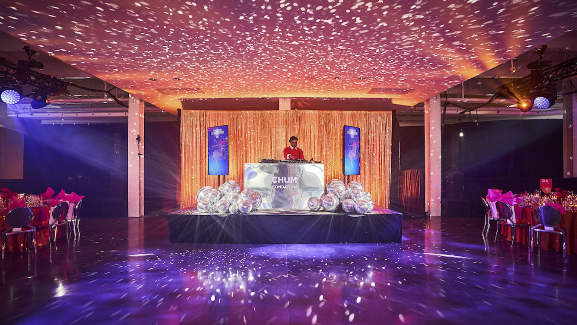 DJ performing at Bal du CHUM gala with chrome DJ booth, large disco ball clusters, and orange drapery at Grand Quay Montreal