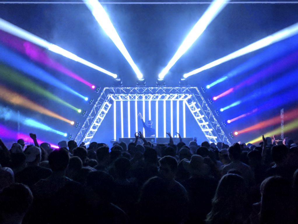 Crowd dancing in front of a custom-built DJ booth with immersive lighting effects, LED structures, and dynamic stage visuals