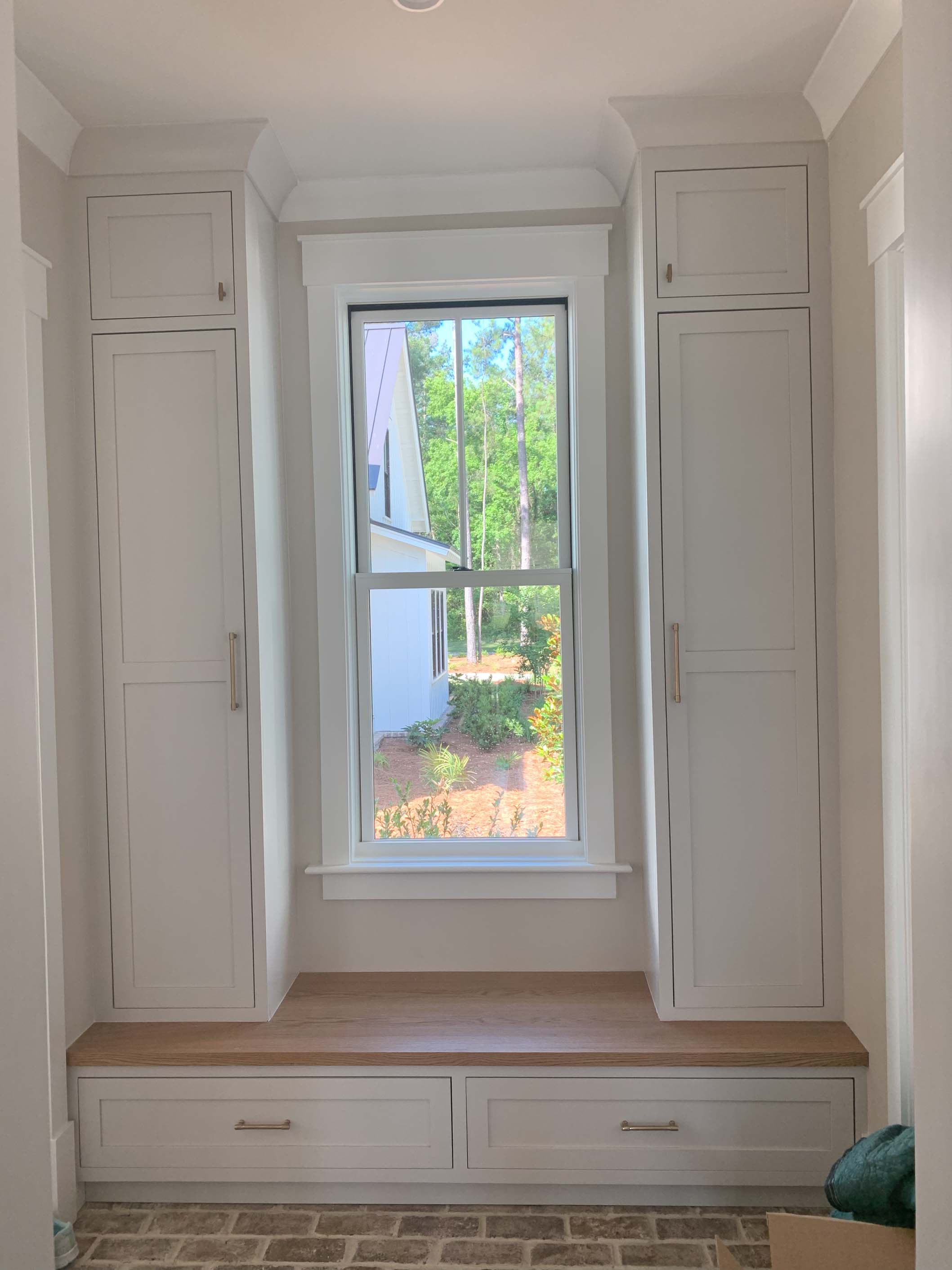 White custom mudroom cabinetry with tall storage and a wood bench beneath the window