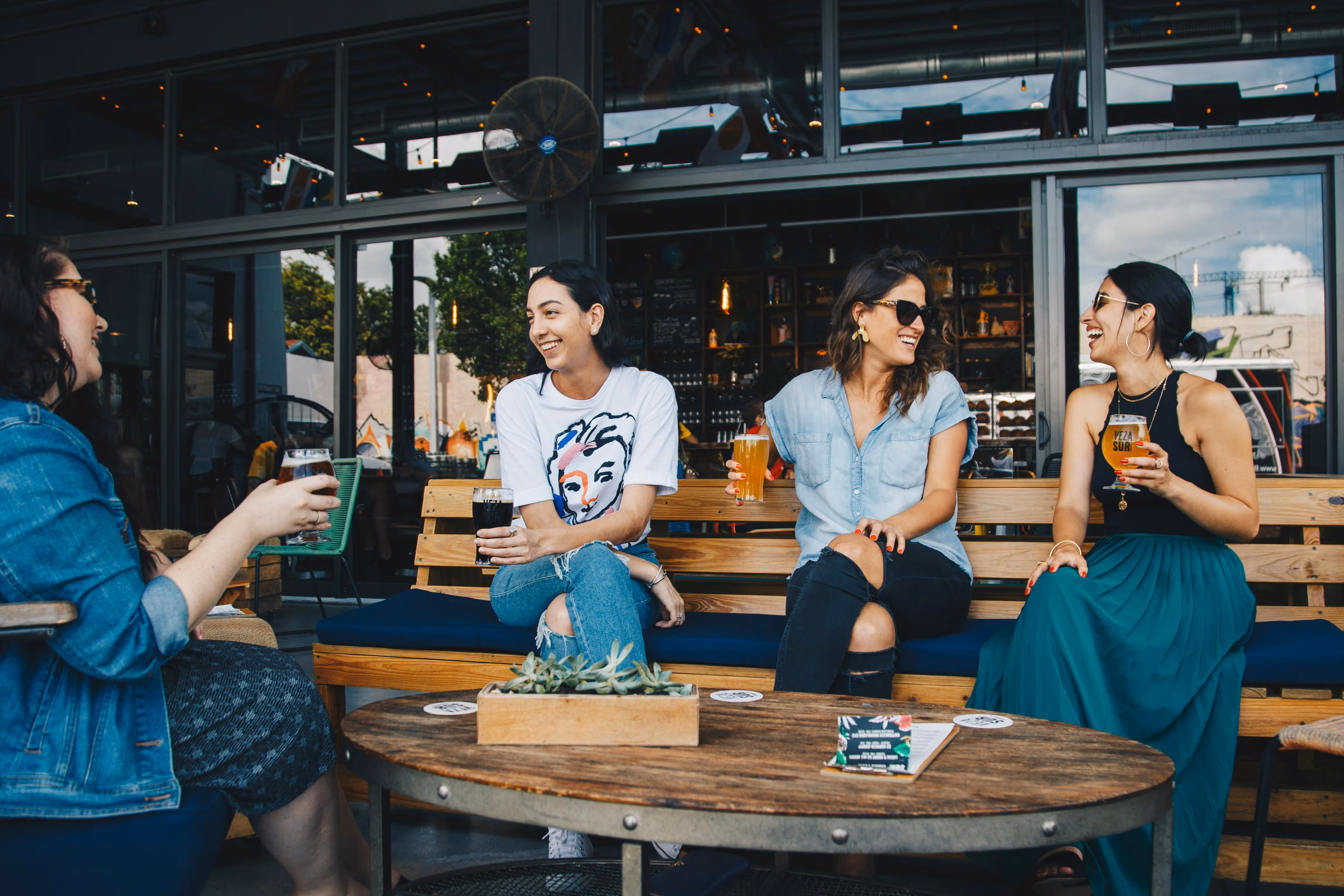 Group of friends enjoying craft beers on the outdoor patio at Old Route 69 Brewery, featuring a lively atmosphere, wooden furniture, and modern taproom backdrop.