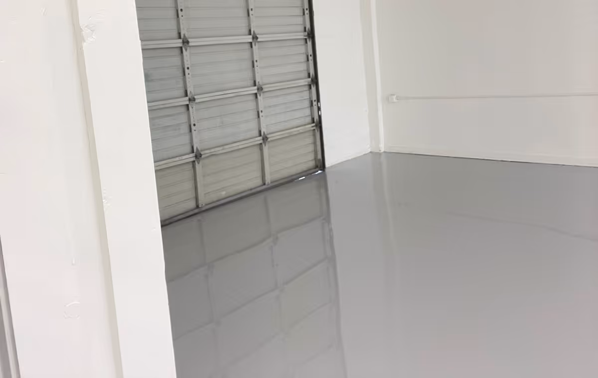 Empty indoor space with shiny light gray epoxy-coated floor and a closed metal roll-up garage door.