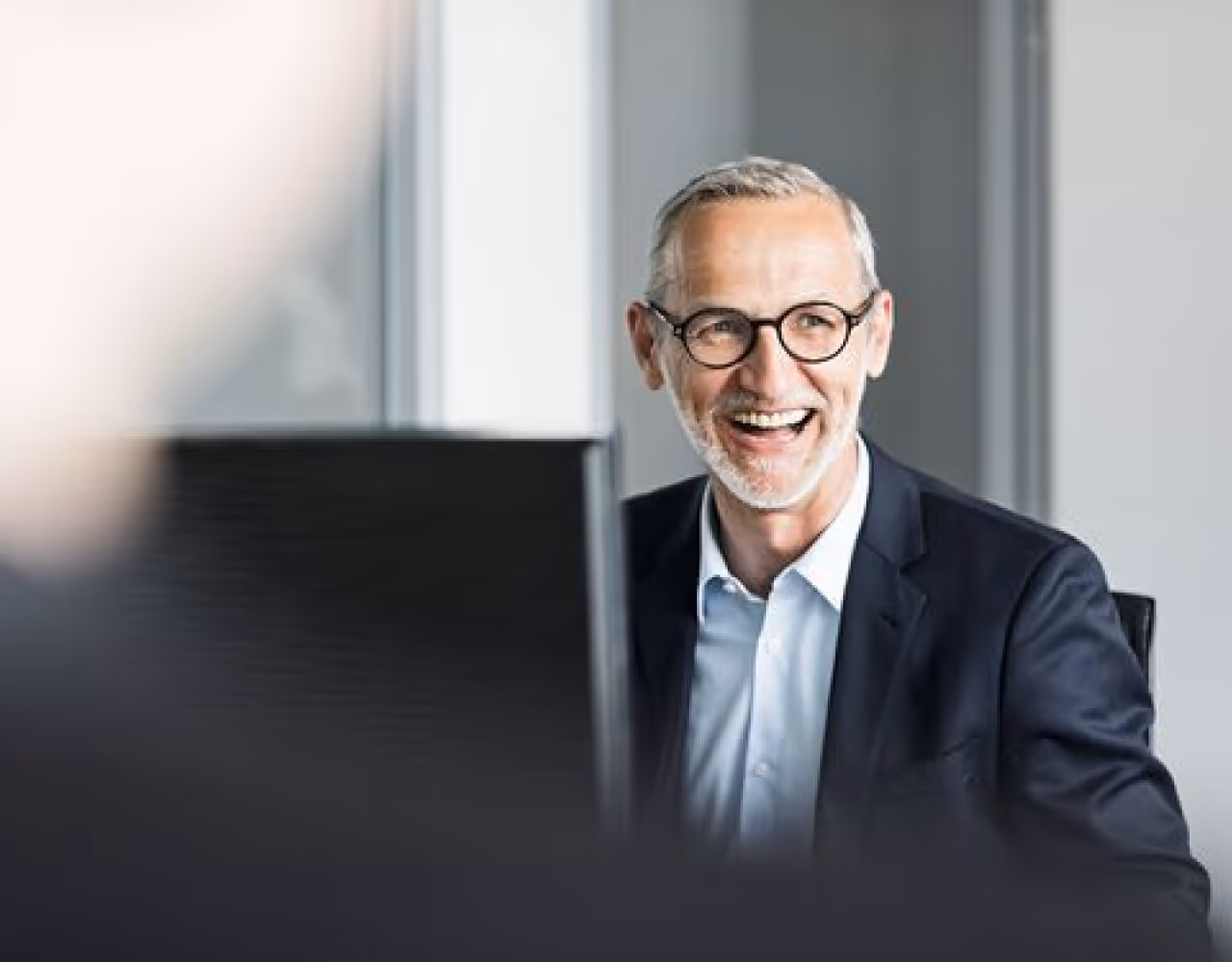 A man wearing glasses and a suit is smiling.